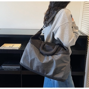 Detail of grey checkered travel tote bag with black handles and detachable shoulder strap