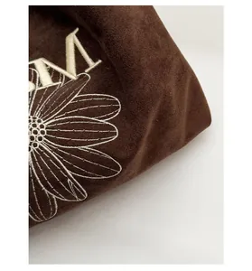 Macro shot of large daisy embroidery and M letter on a premium brown suede tote bag
