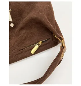 Detail of smooth gold zipper and metallic hardware on brown suede tote bag