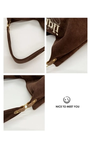 Macro detail of brown suede tote bag showing bronze metal ring and letter embroidery