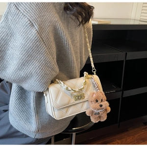 Close-up of white quilted crossbody bag with gold chain and plush dog charm