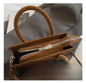 Detail view of brown leather handbag featuring silver metal zipper and stitched handles