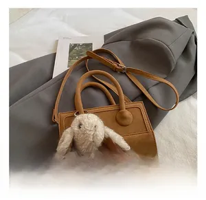 Detail of a brown leather shoulder bag with circular buckle and plush rabbit keychain