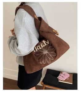 Detailed side view of a brown suede tote bag with daisy embroidery on a model shoulder