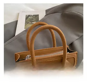Close-up of a brown small square handbag featuring dual cylindrical handles and metal zipper