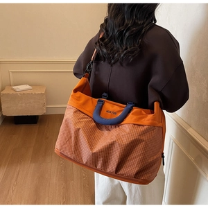 Detail of the large orange travel tote showing the sturdy handles and adjustable strap