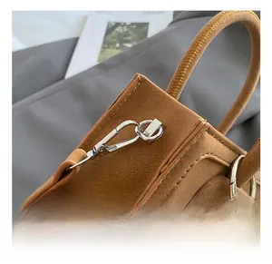 Detail of tan suede handbag showing silver metal hook, stitching, and gray fur ball charm