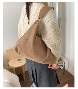 Detail of a brown suede tote bag with floral embroidery and Happy text on shoulder