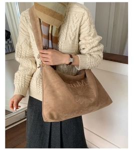 Detail of brown suede tote bag with daisy and MAP embroidery worn with a beige sweater