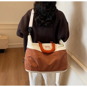 Detail of orange plaid tote bag with adjustable strap shown on model for size reference