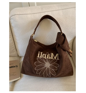 Detail of brown suede tote bag featuring white daisy embroidery and a decorative side bow