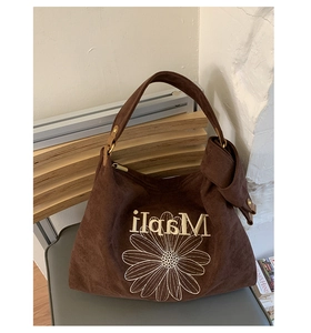 Detail of brown suede tote bag featuring white daisy embroidery and soft leather texture