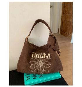 Detail of brown suede tote bag with daisy embroidery and brass hardware on books
