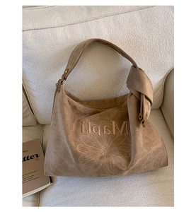 Macro shot of brown suede tote bag with daisy embroidery and wide shoulder strap detail