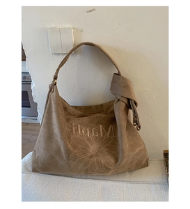 Detail of a brown suede tote bag featuring a floral embroidery and a unique knotted shoulder strap