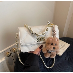 Close-up of white quilted chain shoulder bag featuring gold clasp and plush dog charm