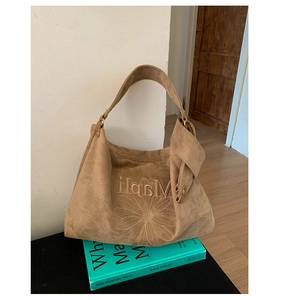 Detail of a brown suede hobo bag featuring white daisy embroidery and a wide strap
