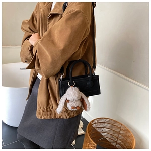 Close-up of minimalist black matte leather square bag with cute grey plush bunny charm
