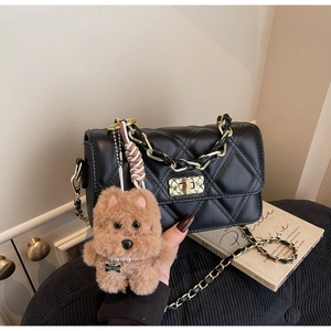 Detail of black quilted crossbody bag with gold lock and plush puppy charm accessory