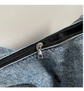 Close-up of a smooth silver metal zipper on a blue denim crossbody dumpling bag