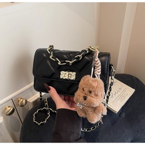 Close-up of black quilted shoulder bag with gold chain and cute dog charm pendant