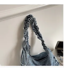 Detail of blue denim hobo bag featuring pleated ruched shoulder strap and zipper closure