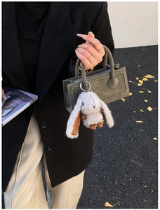 Close-up of a plush long-eared rabbit charm hanging on a green square handbag