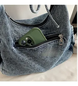 Detail of light blue denim half-moon bag featuring functional front zipper pocket