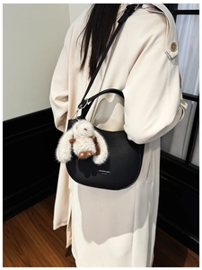 Détail du sac demi-lune en cuir noir texturé avec pendentif lapin blanc en peluche