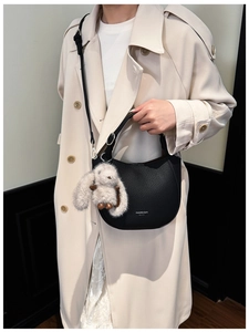 Détail d'un sac seau en cuir noir avec breloque lapin en peluche sur un trench beige