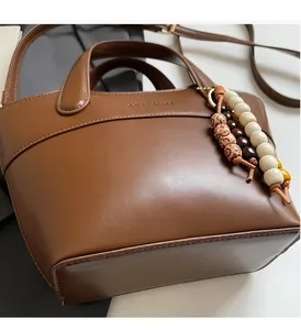 Detail einer braunen Ledertasche mit Holzperlenanhänger und Logoprägung