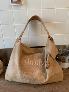 Brown suede Hobo bag featuring daisy embroidery and Mapli lettering on white tile background