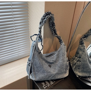 Detail of washed denim shoulder bag featuring ruffled strap and round metal buckle