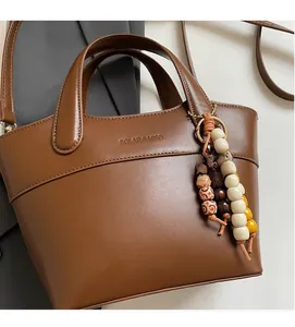 Detailansicht der braunen Ledertasche mit Perlenanhänger und geprägtem Markenlogo