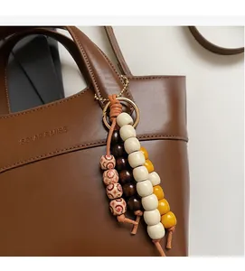 Detail eines bunten Perlenanhängers mit Holzperlen und Goldring an Ledertasche