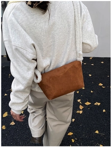 Detail of caramel brown suede shoulder bag with plush cream strap in autumn street setting