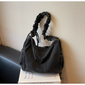 Detail of black washed denim crossbody bag featuring cloud pleat strap and side pockets