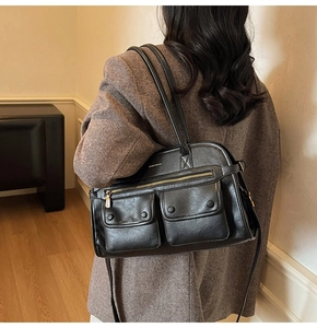 Detail of black faux leather tote bag showing two magnetic front pockets and gold zippers