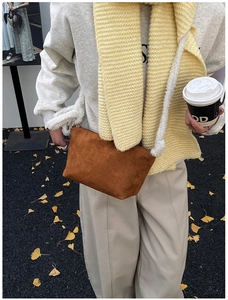 Close-up of brown suede bucket bag with white plush shoulder strap in autumn setting