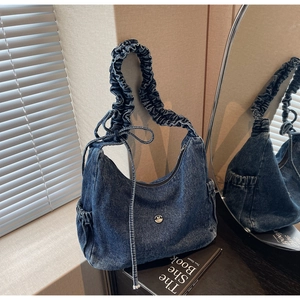 Detail of blue denim hobo bag featuring a gathered strap and metal M logo on mirror surface