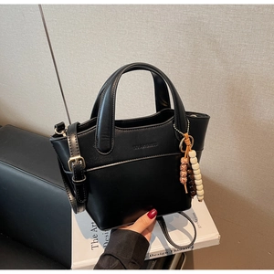 Detailansicht der schwarzen Leder-Eimertasche mit Boho-Perlenanhänger und Goldbeschlag
