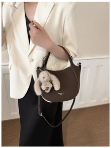 Détail d'un sac demi-lune en cuir marron avec breloque lapin en peluche et bandoulière réglable