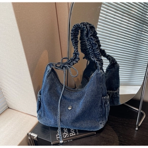 Close-up of denim dumpling bag with pleated shoulder strap and side drawstring bow detail