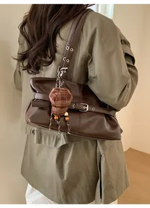 Detail of dark brown leather hobo tote bag featuring buckle strap and plaid hat charm