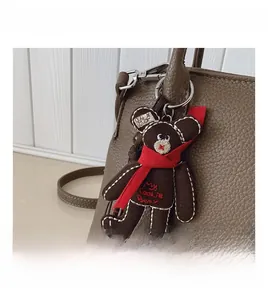 Close-up of brown plush bear charm with red scarf and silver hook on leather bag