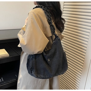 Detail of ruffle shoulder strap and silver metal buckle on a dark grey denim hobo bag