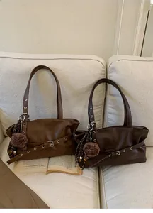 Close-up of vintage brown leather tote bags with multi-hole buckle detail and plaid charm