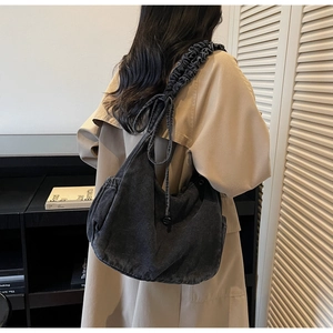 Detail of dark grey denim hobo bag featuring pleated shoulder strap and side bow knots