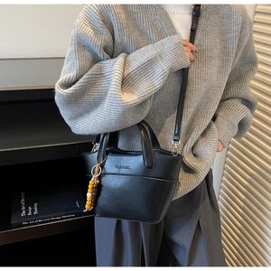 Details der schwarzen Eimertasche aus Leder mit Perlenanhänger und Markenschriftzug