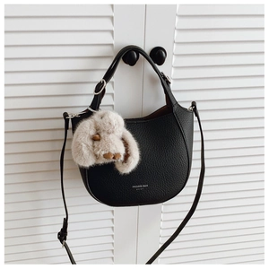 Détail du sac seau en cuir noir grainé avec breloque lapin en peluche sur une porte blanche